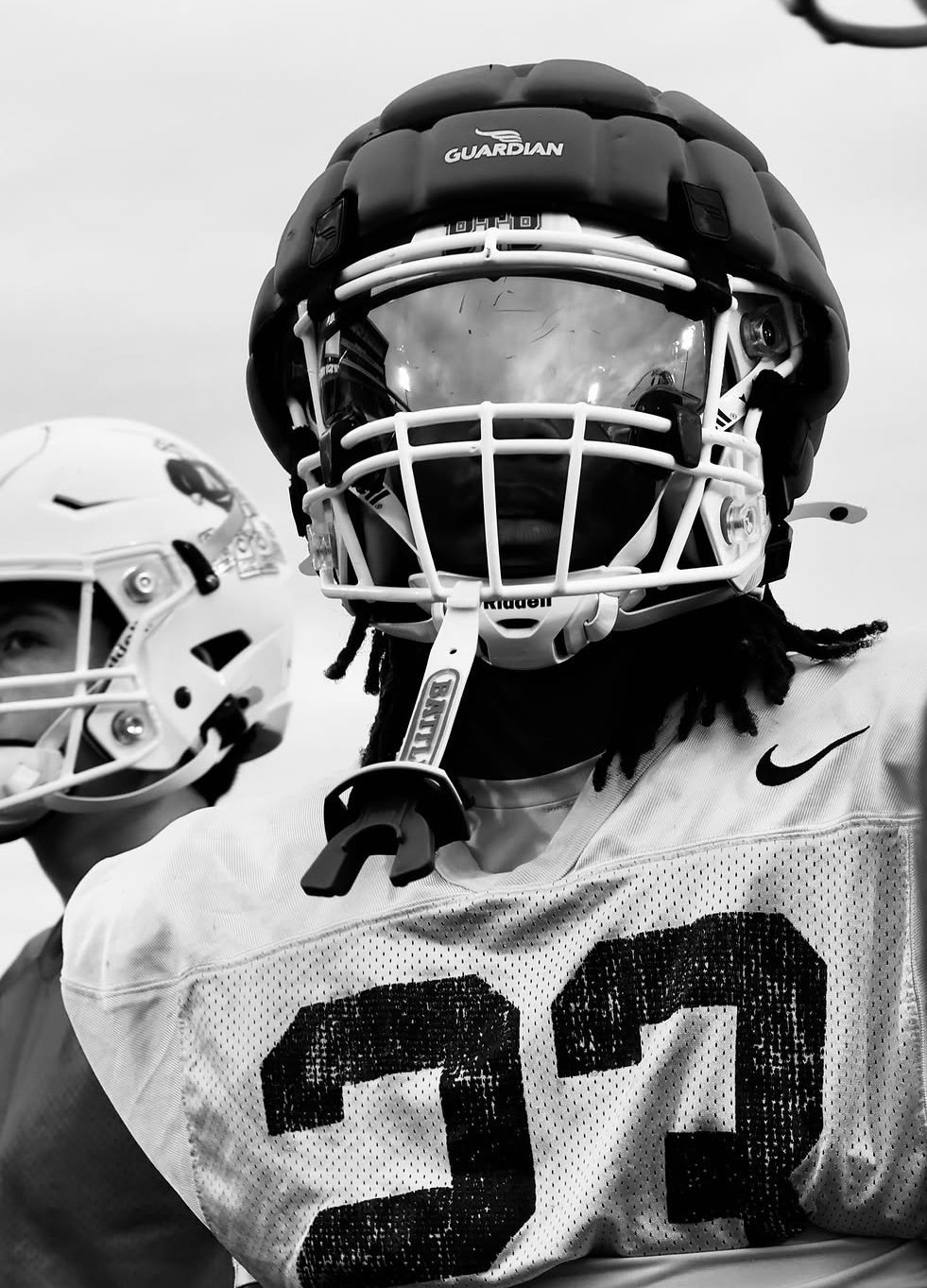 Football player wearing black Guardian helmet and white jersey with number 23, holding helmet in black and white photo