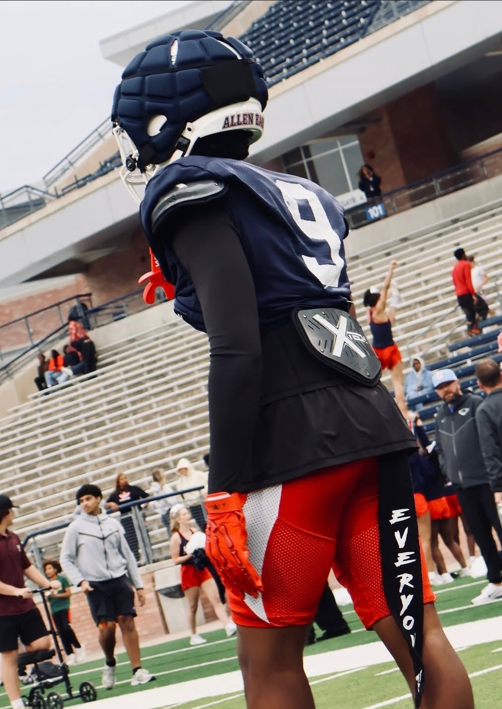 Football player wearing navy and red uniform with helmet standing on stadium field during team practice or game day