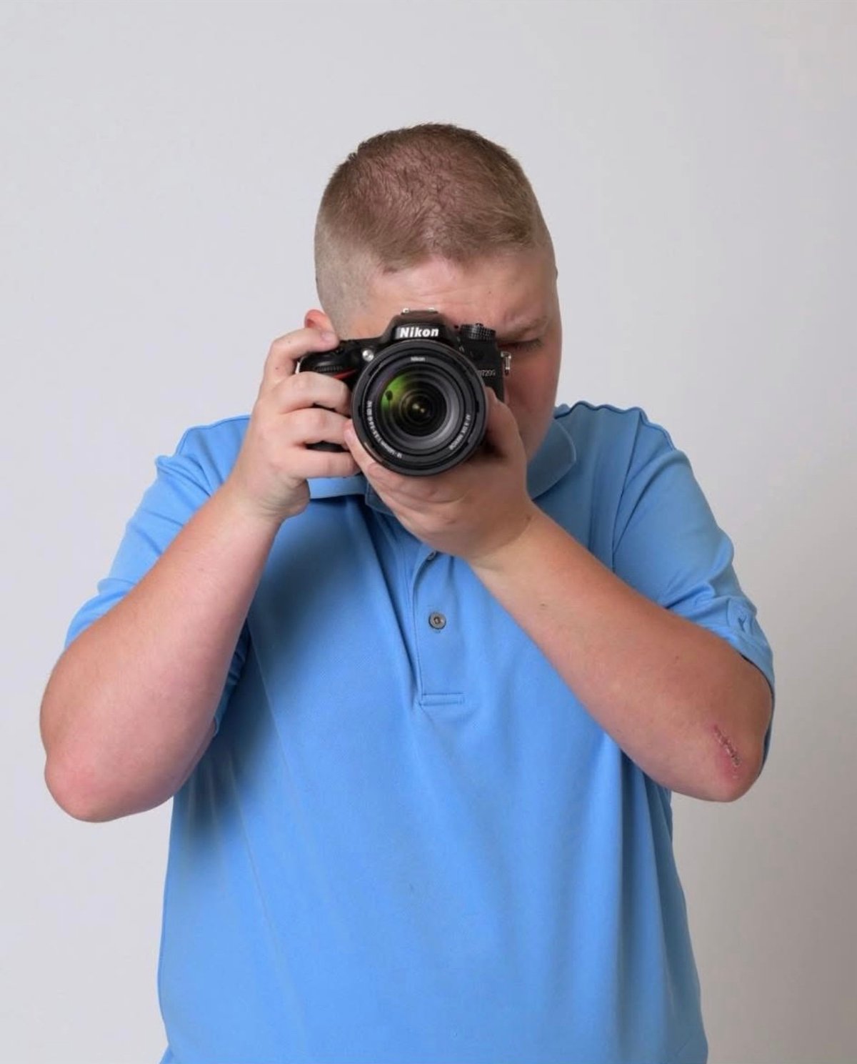 Person in blue shirt holding Nikon camera up to face, ready to take a photo